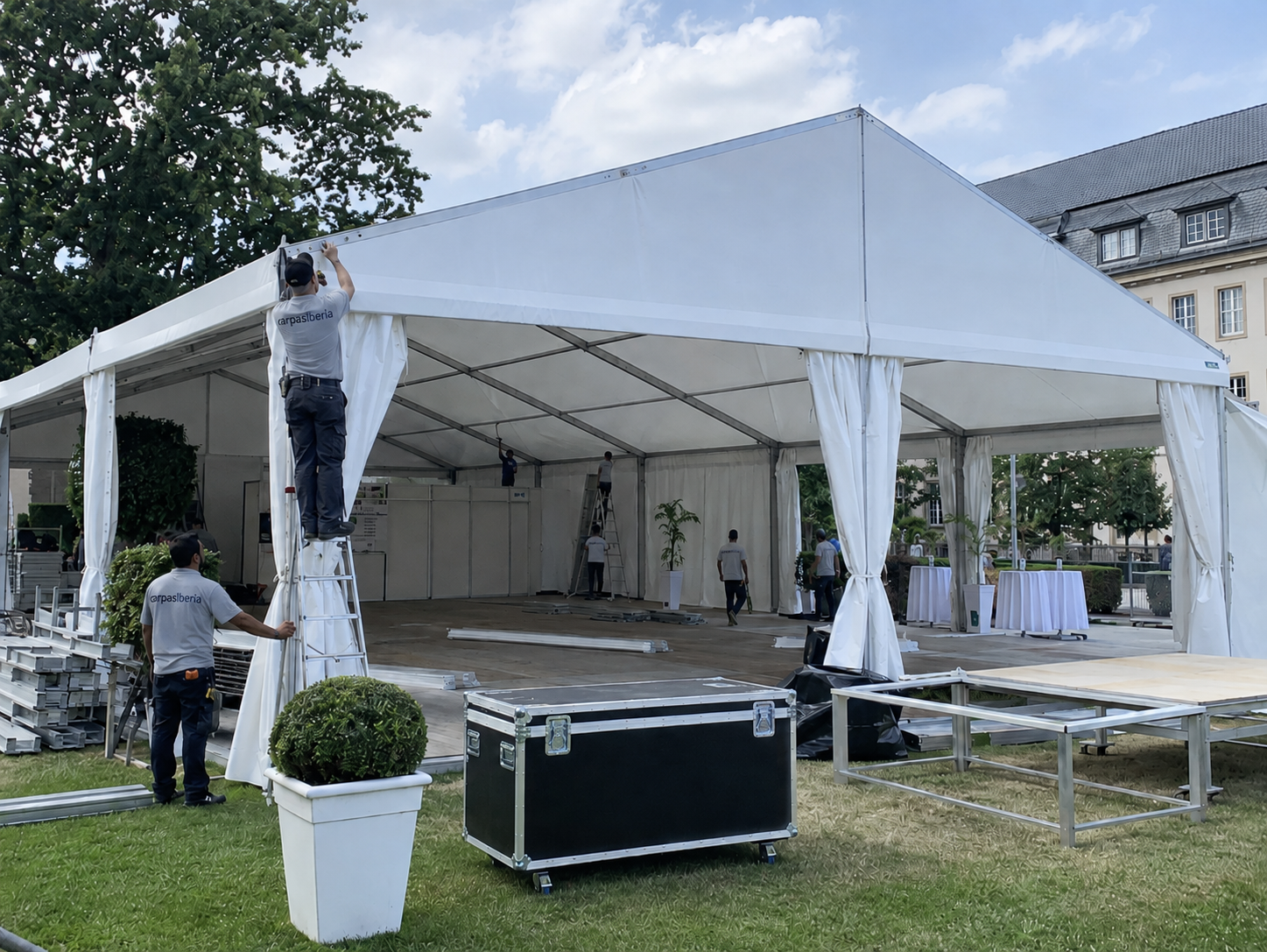 Equipo montando una carpa modular blanca con suelo técnico y laterales abiertos en un jardín