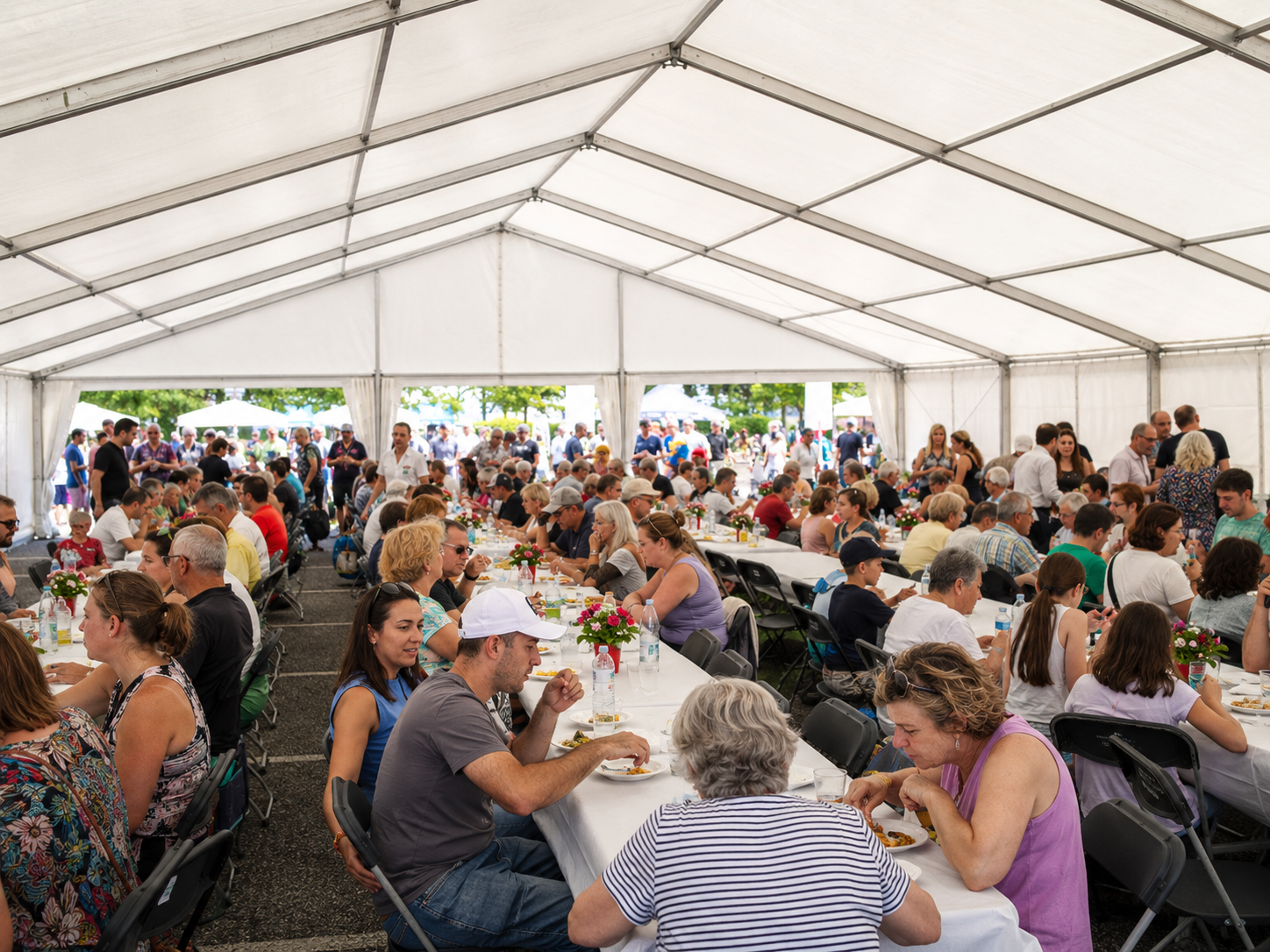 Interior de carpa modular blanca con mesas corridas, comensales disfrutando de una comida popular y centros florales