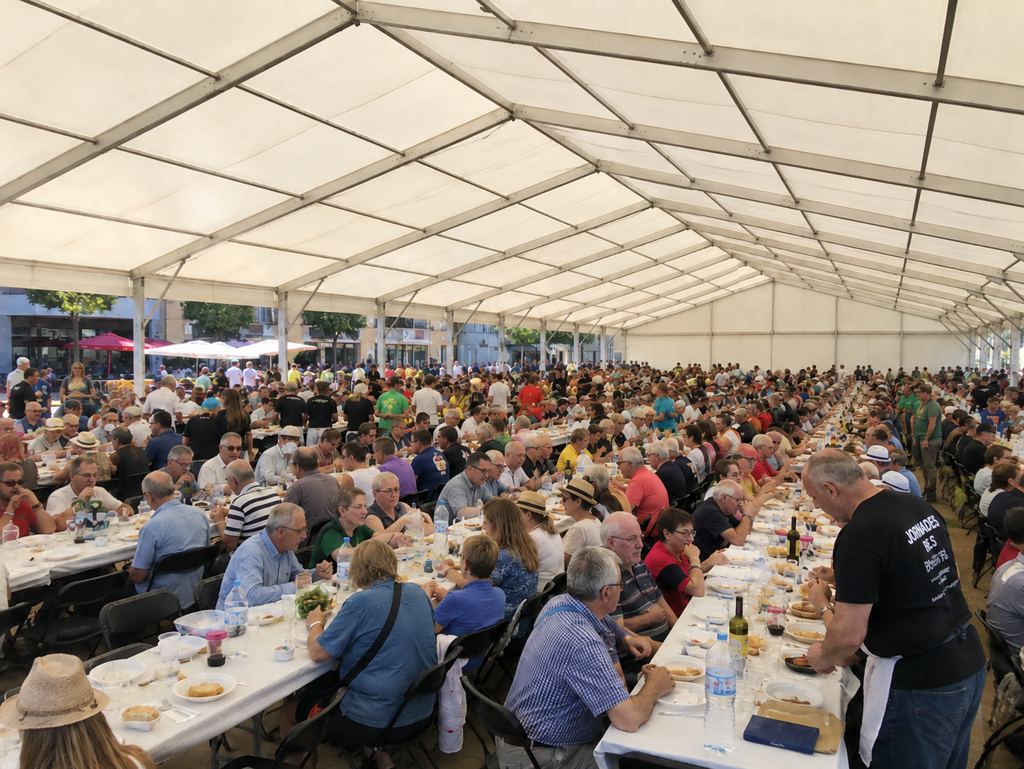 Carpa modular blanca de gran formato con larguísimas mesas de banquete y cientos de comensales en una plaza