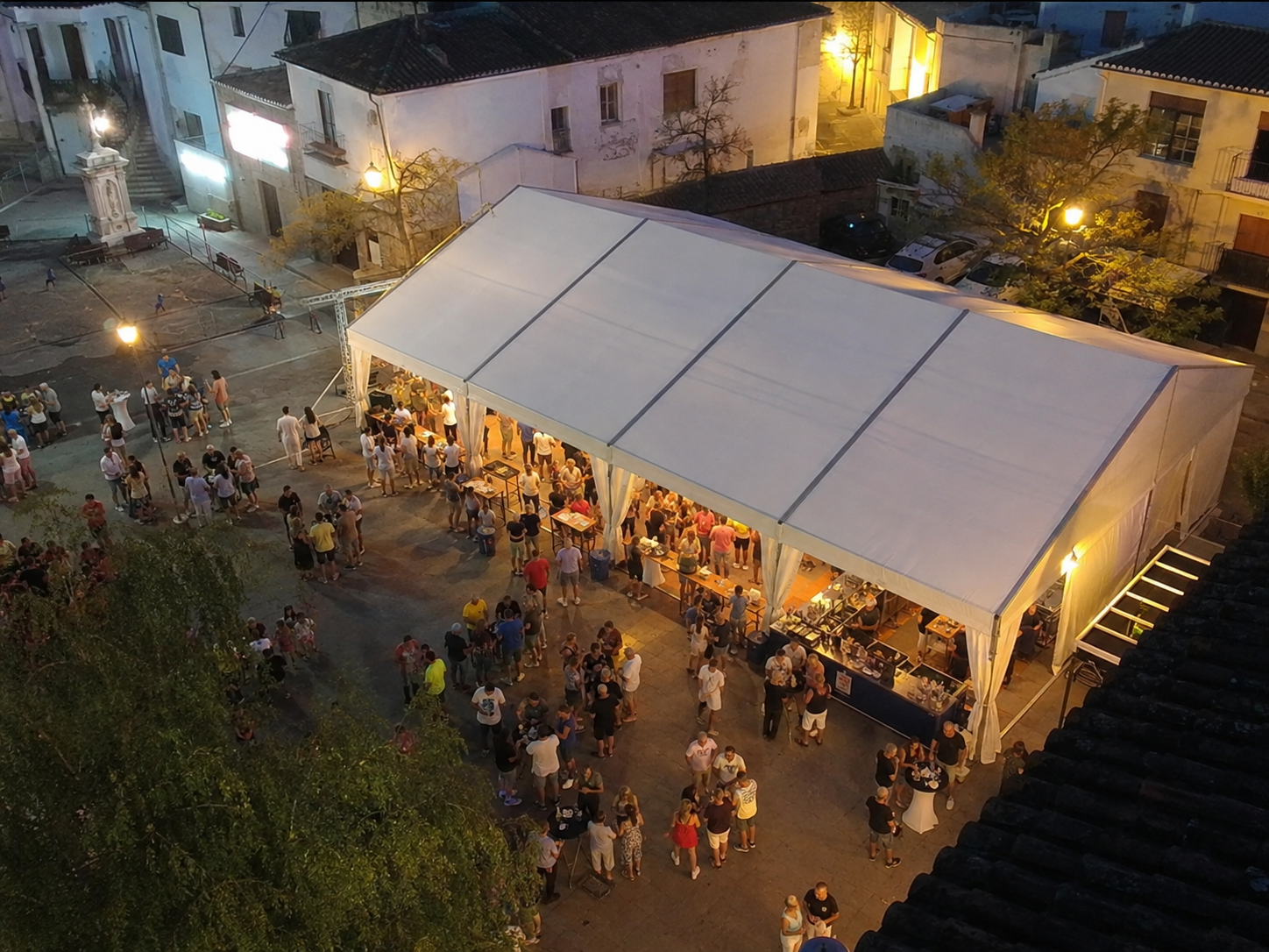 Carpa modular blanca vista desde arriba en una plaza con barra, mesas altas y asistentes al atardecer
