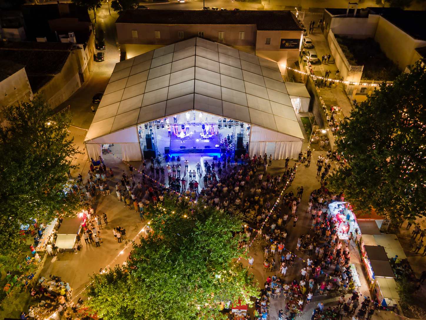 Vista aérea de una carpa modular blanca iluminada durante un concierto nocturno con público alrededor